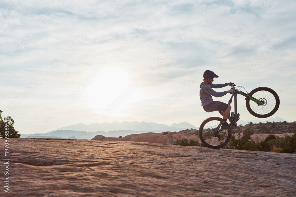 Obraz premium Man, mountain bike and wheelie with exercise in nature for extreme sports, cycling and space for tricks. Person, bicycle and cardio training for stunt, safety gear or speed on ride in countryside