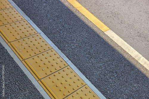 Картината върху платно Yellow tactile paving tiles for the visually impaired on a gray asphalt train station platform, ensuring safety and accessibility for commuters