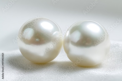 Two large, lustrous pearls rest gently upon a softly draped, white fabric
