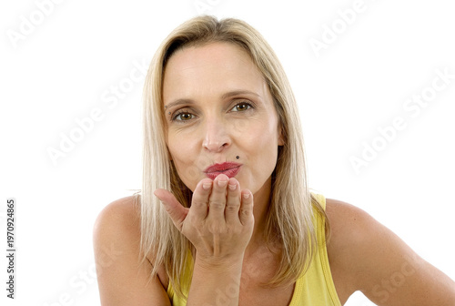 Woman blows kiss with hand near lips. Blonde hair, yellow top, white background. Friendly expression, isolated portrait shot