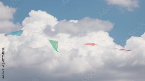 Colorful bunting flags swaying in wind under fluffy cloudy sky