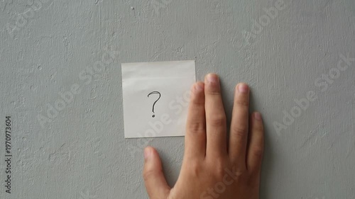 Hand sticking a question mark note on a gray wall