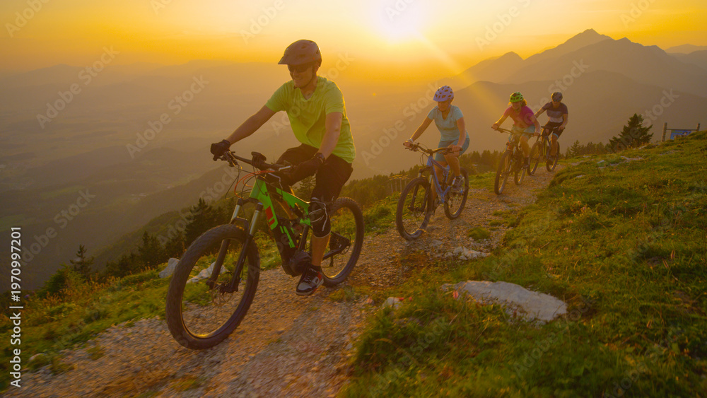 Obraz premium DRONE: Group of tourists riding electric bicycles up a scenic trail at sunset.