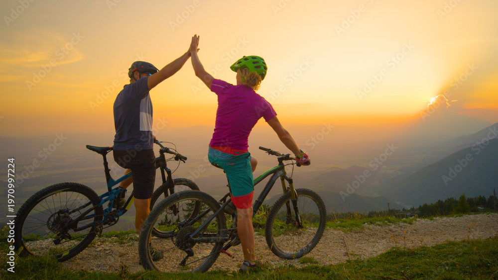 Fototapeta premium COPY SPACE: Cheerful friends high five at sunset after successful bicycle ride.