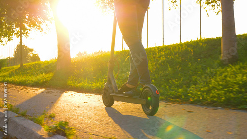 LOW ANGLE: Cinematic shot of a woman in jeans riding an e-scooter at sunset.