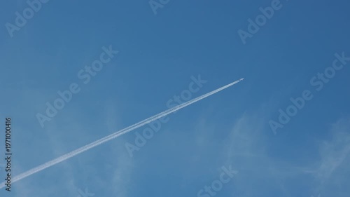 Airplane leaving long white condensation trail in clear blue sky