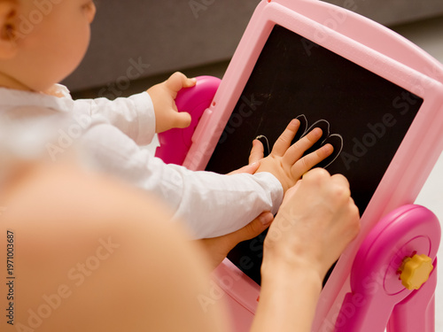 Quadro em tela A mom carefully outlines her little boy's hand with chalk on a blackboard