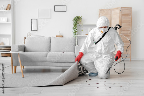 Tableau sur toile Pest control worker in protective suit spraying insecticide under carpet during