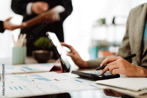Young colleagues discuss business and analytical price charts using calculators and laptops to calculate financial, tax, accounting, statistics and analytical research ideas.