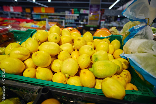 Lemons are piled high in a green basket at a grocery store