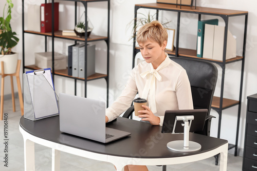Mature businesswoman with coffee cup working at table in office