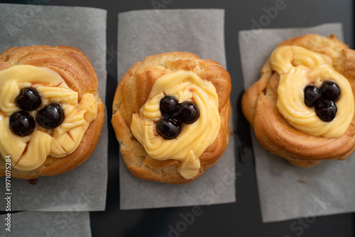 High-angle shot of traditional Italian Zeppole di San Giuseppe, handmade and fresh from the oven. The pastries are resting on a rustic black baking sheet lined with parchment paper, showcasing the gol