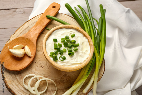 Foto Bowl of tasty sour cream with sliced scallion and onion on grey wooden backgroun
