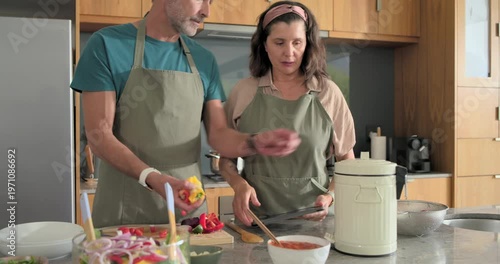 Couple in aprons using tablet in kitchen chopping on cutting board opening cooker preparing meal