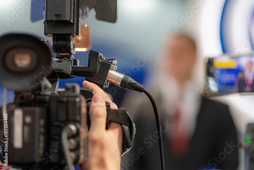 Recording an interview using a professional camera connected to an external audio cable. Integrated audio-video capture supports clear communication and accurate media reporting.