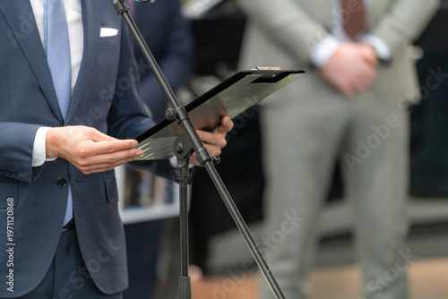 Reading prepared notes while speaking at a media event using a microphone stand. Structured delivery supports clarity, accuracy, and effective communication in professional settings.