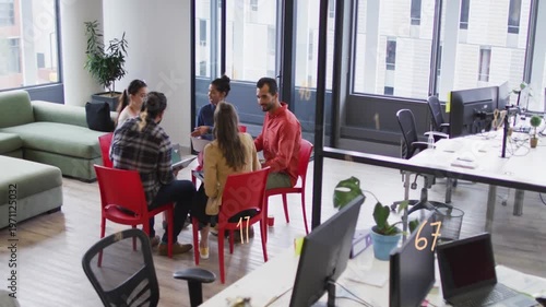 Five coworkers exchanging looks, plaid speaker turning and gesturing, group leaning in to plan