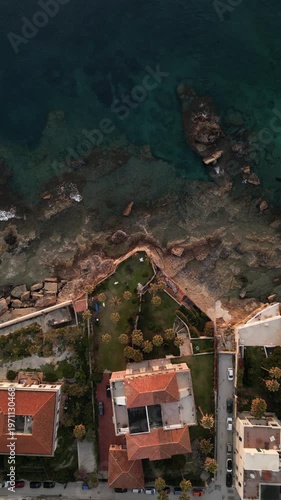 Aerial view of Italian coastline at dawn, showcasing rocky shoreline, coastal homes, and lush gardens along the clear blue waters of the Mediterranean Sea