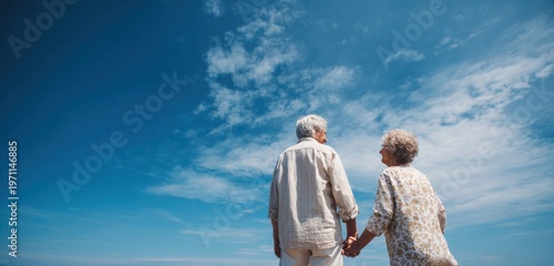 Wallpaper Mural Elderly couple standing outdoors under a vibrant blue sky with scattered white clouds, holding hands, enjoying a serene moment together Torontodigital.ca