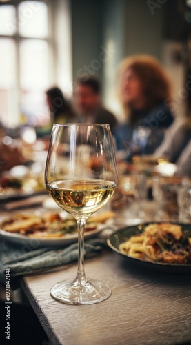 Wallpaper Mural Elegant glass of white wine with a smooth, clear texture and pale golden hue on a dining table amidst a social gathering with food and blurred guests in the background Torontodigital.ca