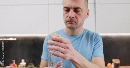 Thoughtful man studies plastic bottle touching cap before recycling step begins. Person checks container shape deciding separating lid for proper sorting