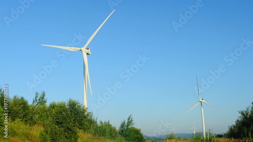 Powerful wind turbines work at countryside industrial farm under blue sky. Clean way to produce electricity safely for environment slow motion