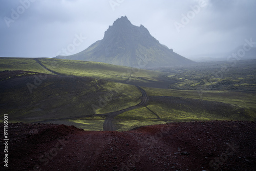Dominant solitary volcanic mountain with clouds above surrounded by green lichen fields, Iceland