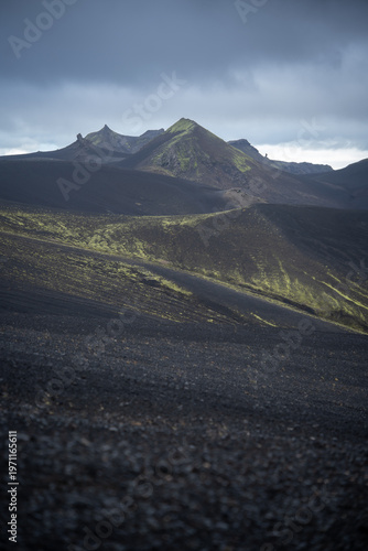 Vertical shot of volcanic landscape with mountains covered by black sand and green lichen, Iceland