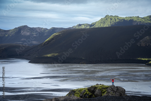 Hiker in the distance enjoying views on mountainous volcanic landscape with glacial river, Iceland