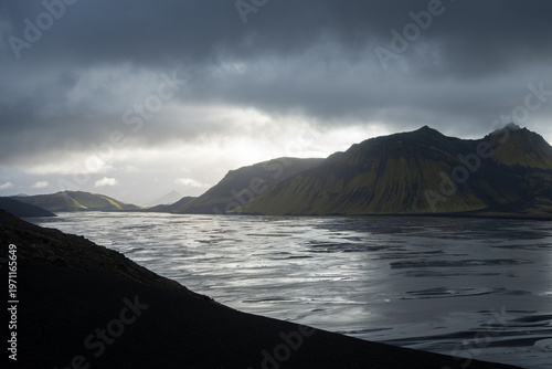 Sun setting behind mountains in glacial landscape with heavy storm clouds above, Iceland