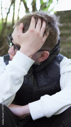 Sad teenage boy sitting outdoors after school, feeling lonely and thoughtful. Vertical video.