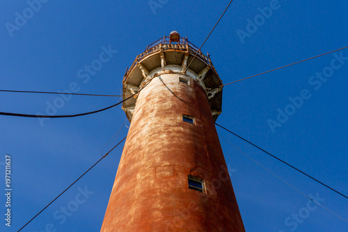 Low angle view of historic rusty metal lighthouse tower against clear blue sky. Industrial heritage and maritime navigation structure in a coastal city. Sukhumi, Abkhazia.