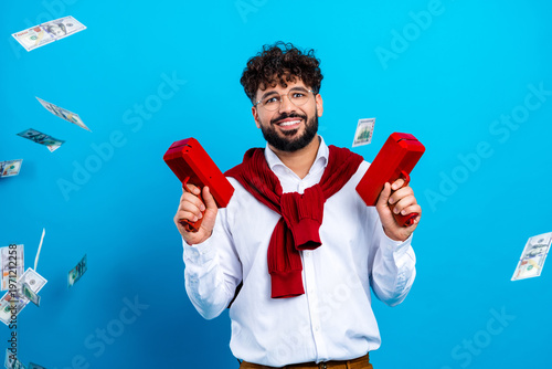 Fotografie Smiling man with money guns celebrating cash windfall on blue background, happy