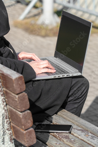 Woman typing on laptop with blank screen for UI mockup on park bench