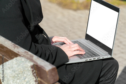 Woman typing on laptop with white blank screen for UI mockup on park bench