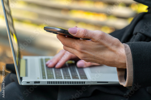 Woman holding smartphone for two-factor authentication near laptop outdoors