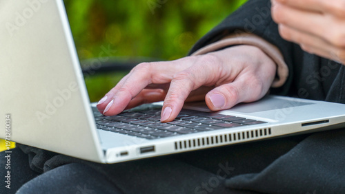 Woman typing on laptop keyboard for digital nomad copywriting in park