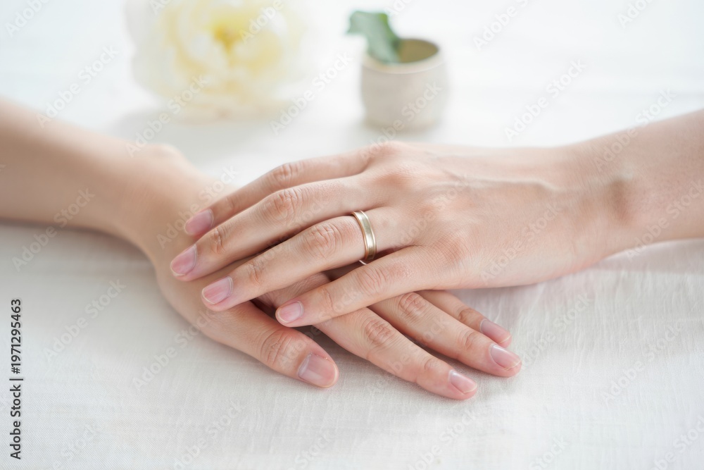 Naklejka premium Elegant Display of Intertwined Hands Showcasing a Ring Against a Soft Floral Background, Symbolizing Love and Connection