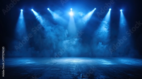 Blue stage lights beam down through fog onto an empty floor, creating a dramatic and atmospheric scene.