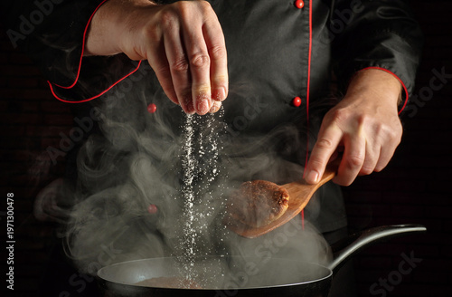 Fotografía A chef sprinkles salt from a hand into a pot on the stove