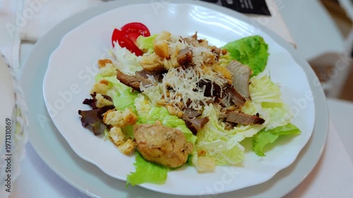 Grilled chicken caesar salad presenting crispy croutons, grated parmesan, ripe tomato slice atop fresh lettuce against pristine white surface