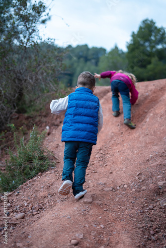 Two children playing and climbing up a dirt hill on a sunny day