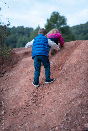 Two children playing and climbing on a dirt hill in a natural outdoor setting
