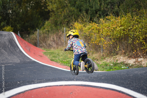 A young boy riding a bike on a paved bike track with a red and white design