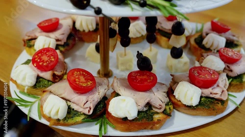 Elegant platter displaying roasted beef, cherry tomatoes, pesto, cheese, olive skewers garnished with fresh rosemary sprigs on multi level serving plate