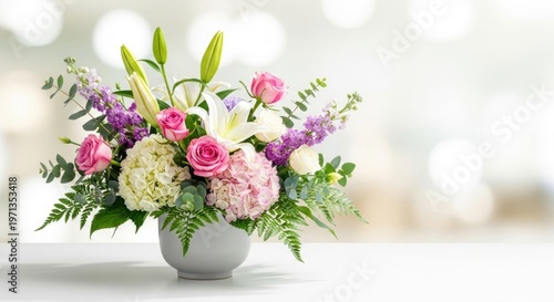 A vibrant flower arrangement with pink roses, white lilies, and purple hydrangeas in a white vase on a white table.