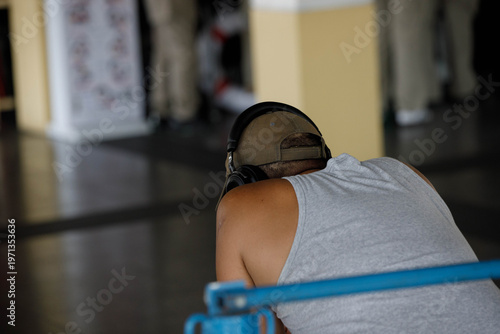 Guy in headphones sitting waiting in boat terminal, human presence in urban environment, public life concept, back view, Tha Chang Pier.