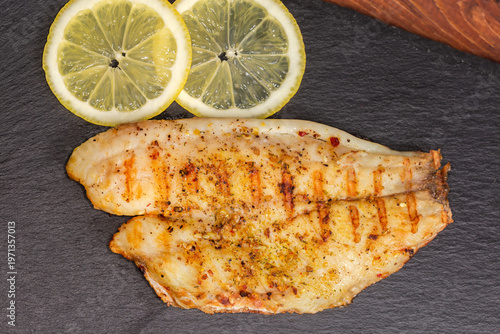 Grilled gilthead fillet with lemon slices on black slate plate