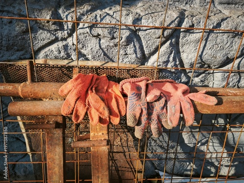 Protective work gloves hanging on metal fence at construction site during building renovation and outdoor repair work