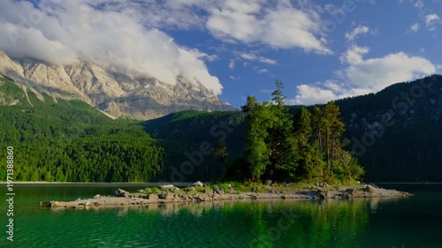 Static shot of a small island in Eibsee lake reflecting the Zugspitze mountains and blue sky in the Bavarian Alps, Germany.
